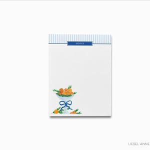 Könnte beinhalten: Ein weißer Notizblock mit blau-weiß gestreiftem Rand. Der Notizblock hat ein blaues Band und das Wort "Sydney" darauf gedruckt. Der Notizblock hat eine Aquarell-Illustration einer Schüssel mit Orangen und Grün.
