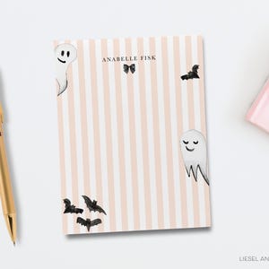 a pink and white striped notebook with a gold pen and a gold stapler on a white background.