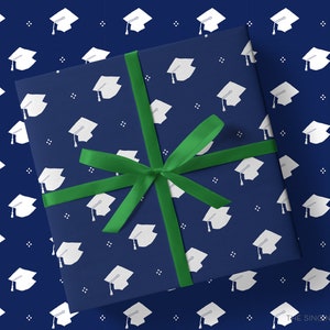 May include: A navy blue gift box with a green ribbon. The box is wrapped in wrapping paper with a white graduation cap pattern.