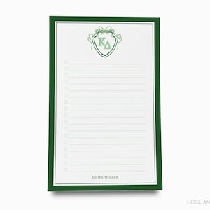 May include: A white notepad with a green border and a green crest featuring the letters K and Δ. The notepad has a list format with checkboxes and the name "EMMA MILLER" at the bottom.