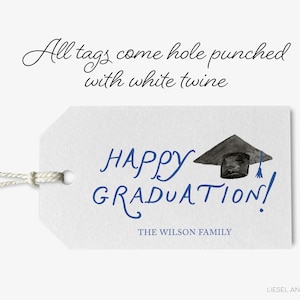 The image is a graduation tag with a graduation cap and mortarboard, accompanied by the text "All tags come hole punched with white twine" and "HAPPY GRADUATION!" The tag also includes the text "THE WILSON FAMILY" and "LIESEL ANNE STUDIOS".