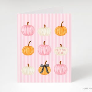 A pink striped card with nine pumpkins of various sizes and colors, including white, orange, and yellow, arranged in a 3x3 grid.
