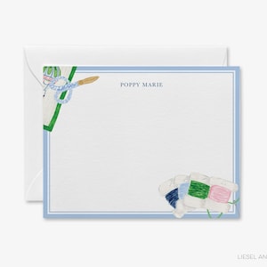 Op de afbeelding: Een witte briefpapier set met een lichtblauwe rand en de tekst "POPPY MARIE". Het ontwerp bevat aquarel illustraties van naai-gereedschap en garenklosjes in blauw, groen en roze.