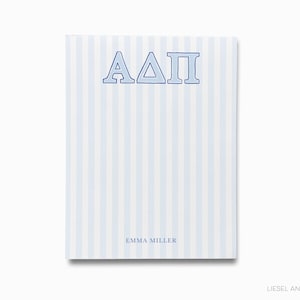 May include: A notepad with a light blue and white striped pattern. The letters "ΑΔΠ" are at the top in blue, with the name "EMMA MILLER" at the bottom. The notepad is rectangular and has a clean, minimalist design.