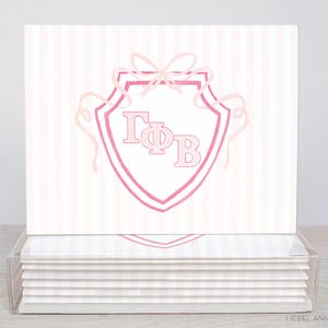 May include: Stationery cards with a pink and white striped design. Each card has a pink shield design with the Greek letters ΓΦB. The cards are presented in a clear acrylic holder.
