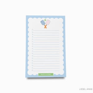 Op de afbeelding: Een blauwe notitieblok met een gegolfde rand en een wit gestreept interieur. De notitieblok heeft een kleine illustratie van twee paddle rackets en een bal bovenaan. De notitieblok heeft de naam "KAYLA AVERY" onderaan gedrukt.