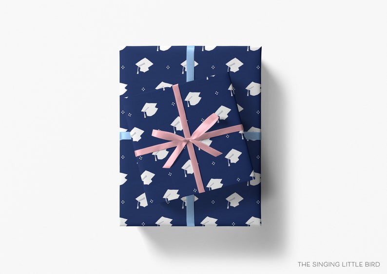 May include: Two navy blue gift boxes with a white graduation cap pattern. The smaller box is wrapped with a pink ribbon and the larger box is wrapped with a light blue ribbon.