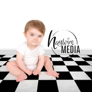 May include: A baby in a white onesie sits on a black and white checkered floor. The baby is looking at the camera. The background is a white wall with a black logo that says "Haywire Media".