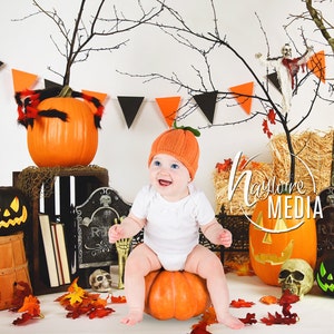 Puede incluir: Un bebé con un gorro de calabaza naranja está sentado sobre una calabaza, rodeado de decoraciones de Halloween. La escena incluye calabazas talladas, una paca de heno, una lápida y hojas de otoño. Banderines negros y naranjas cuelgan en el fondo.