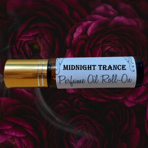 May include: A perfume oil roll-on bottle with a gold cap and a label that reads "MIDNIGHT TRANCE" and "Perfume Oil Roll-On." The bottle is set against a background of dark red flowers.