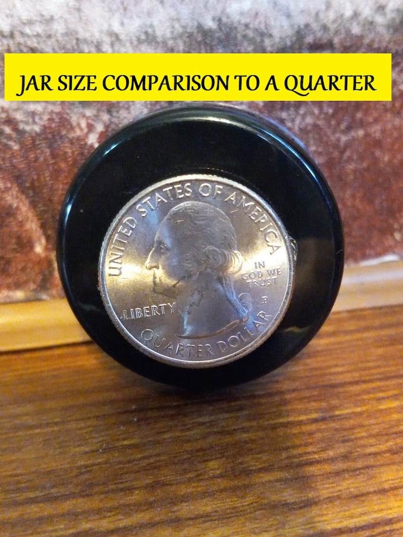 May include: A close-up of a US quarter coin, showing the head of George Washington, with the words "UNITED STATES OF AMERICA", "LIBERTY", "IN GOD WE TRUST", and "QUARTER DOLLAR" inscribed around the edge. The coin is sitting on top of a black jar lid.