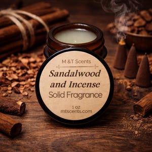 Pode incluir: Um pequeno frasco aberto de fragr&acirc;ncia s&oacute;lida rotulado "S&acirc;ndalo e Incenso" por M & T Scents. O frasco &eacute; castanho com uma tampa preta e um r&oacute;tulo bege. A fragr&acirc;ncia &eacute; de 28g e o site &eacute; mtscents.com. Pauzinhos de canela e cones de incenso no fundo.