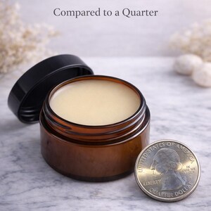 Pode incluir: Um pequeno frasco de vidro castanho aberto preenchido com um b&aacute;lsamo s&oacute;lido amarelo claro, ao lado de uma moeda de vinte e cinco centavos americana. O texto "1 oz Solid Balm Compared to a Quarter" est&aacute; acima do frasco. O frasco tem uma tampa preta.