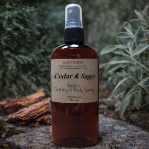 May include: An amber-colored plastic spray bottle with a black nozzle and a tan label. The label reads M & T SCENTS, Cedar & Sage, Room, Clothing & Body Spray, mtscents.com, and 4.5 fl. oz. The bottle has a clear cap and a cylindrical shape.