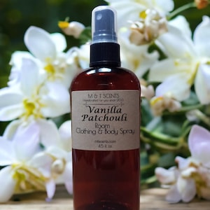 May include: A brown glass bottle with a black spray nozzle and a brown label that reads "M&T SCENTS Handcrafted for you since 2013 Vanilla Patchouli Room Clothing & Body Spray mtscents.com 4.5 fl oz".