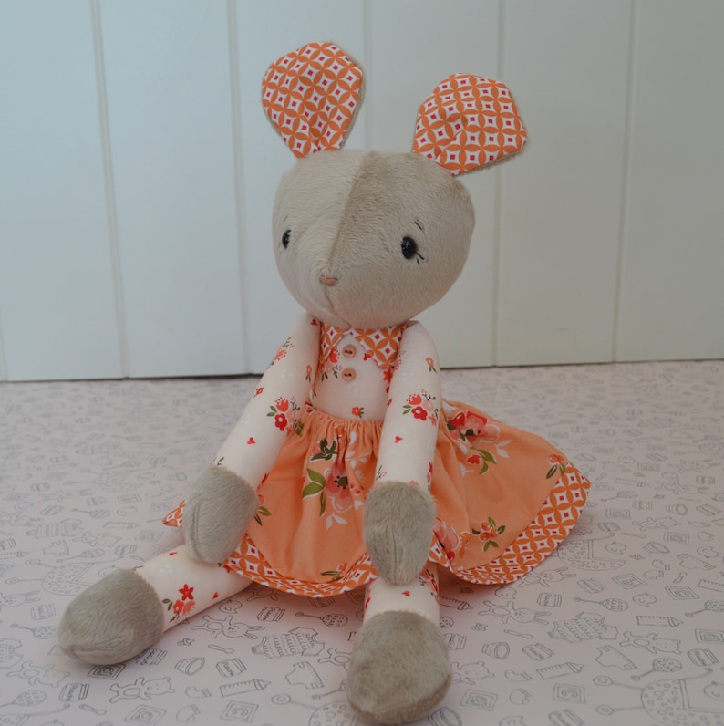 May include: A plush toy mouse wearing a peach-coloured dress with floral print and orange and white geometric patterned ears.