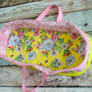 May include: A pink and yellow fabric tote bag with floral print and white polka dots. The bag has two handles and is empty.
