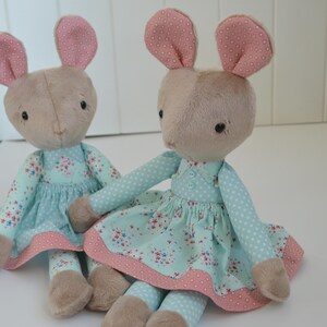 May include: Two plush toy mice wearing light blue dresses with pink floral patterns and white polka dots. The mice have pink ears and brown fur.