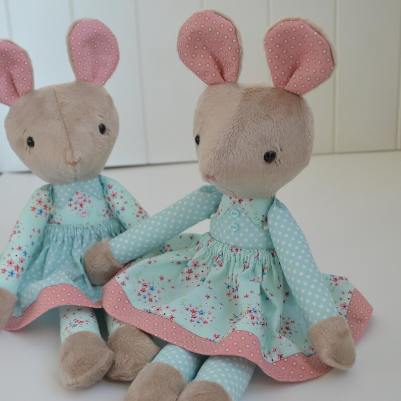 May include: Two plush toy mice wearing light blue dresses with pink floral patterns and white polka dots. The mice have pink ears and brown fur.