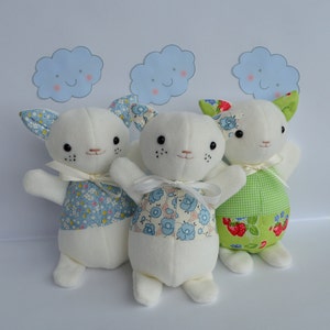 May include: Three white plush cat toys with different fabric patterns. The cat on the left has a blue and white floral pattern, the cat in the middle has a blue and white floral pattern, and the cat on the right has a green and white checkered pattern with red strawberries.