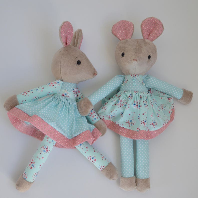 May include: Two plush toy mice wearing blue and pink dresses with floral patterns. The mice have brown fur and long, floppy ears.