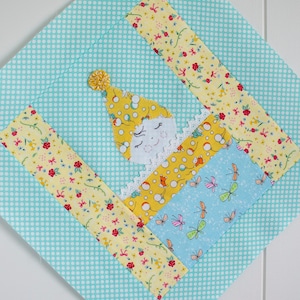 May include: A patchwork quilt block with a whimsical design featuring a sleeping character with a yellow hat and a blue and yellow bed. The block is surrounded by a turquoise background with white polka dots.