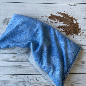 May include: A blue and gray fabric pillow filled with flax seeds. The pillow has a white floral pattern and a label that reads "Sleepytime".