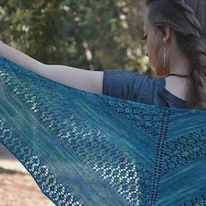 May include: A triangular knit shawl in shades of teal, turquoise, and deep blue. The textile features a delicate openwork lace pattern with intricate stitch details throughout the fabric, creating a textured appearance across the entire surface.
