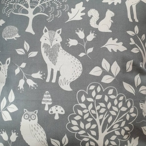 Peut inclure: Un tissu gris avec un motif de forêt blanc. Le motif comprend un renard, un hibou, un écureuil, un cerf, des arbres, des champignons et des feuilles.