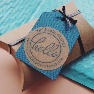 May include: A brown cardboard box tied with a black ribbon, with a blue tag and a round sticker that says "hello". The tag and sticker have the shop name "The Pearl Clutch" and the Etsy shop URL.