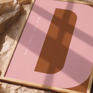 Può includere: Stampa incorniciata con una grande lettera "D" marrone su sfondo rosa. Include il nome "Daniel", data, peso e altezza in cm. La cornice in legno aggiunge un tocco naturale. L'altezza è di 49,6 cm.