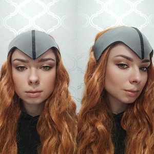 May include: A gray headpiece with a black stripe down the center. The headpiece is worn on the forehead. The person in the image has long, wavy red hair.