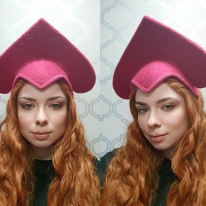 May include: A magenta-colored hat with a heart-shaped crown and a decorative stitched edge. The hat is made of felt and has a unique, pointed design. The hat is a fashion accessory.