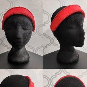 May include: A red headband with a wide band and a narrow, decorative trim. The headband is displayed on a black mannequin head, showcasing its design from multiple angles. The trim appears to be a darker shade of red.