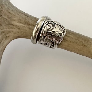 May include: A silver ring made from a repurposed vintage spoon with an ornate design featuring a woman's face and floral motifs.