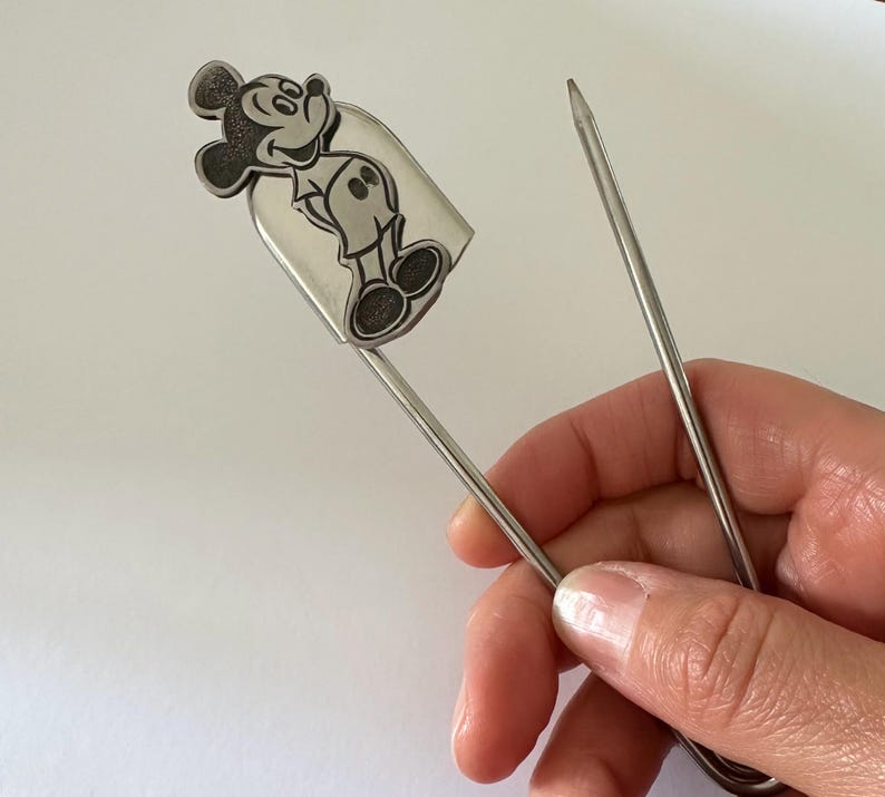 Pu&ograve; includere: Segnalibro color argento con un'illustrazione dettagliata di Topolino. Il segnalibro &egrave; tenuto in mano, mostrando la silhouette del personaggio. Il segnalibro &egrave; realizzato in metallo sottile e resistente. Un accessorio utile.