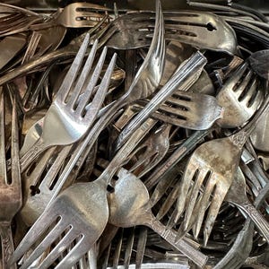 May include: A close-up of a pile of silver forks. The forks are all different styles and sizes, and some have ornate designs.