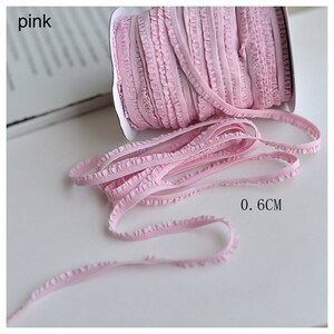 Pu&ograve; includere: Finitura elastica rosa con volant, larga 0,6 cm, avvolta su un rotolo.