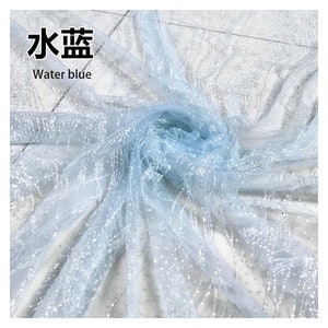 Può includere: Tessuto di tulle azzurro chiaro con glitter argentati. Il tessuto è trasparente e ha una texture delicata. Il testo "Water blue" è scritto in nero su sfondo bianco.