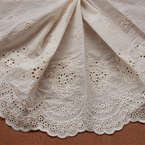 May include: White cotton fabric with a delicate eyelet lace trim. The fabric has a floral pattern with small holes throughout.