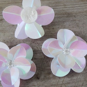 May include: Three iridescent pink and white flower-shaped sequins with a pearl-like center.