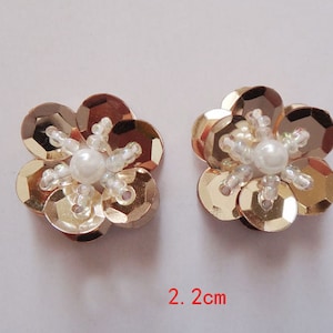 May include: Two gold flower-shaped embellishments with a pearl center. Each flower is approximately 2 inches in diameter.