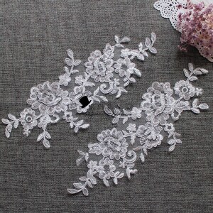 May include: Two white lace appliques with floral designs. The appliques are made of delicate lace and feature intricate floral patterns.