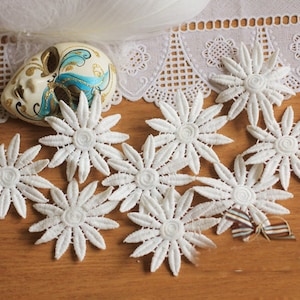 May include: White lace flower appliques, perfect for adding a touch of elegance to crafts and clothing projects. The appliques are delicate and intricate, with a raised center and multiple layers of lace.