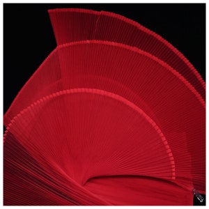 May include: A red fabric fan with pleats, folded in a spiral shape. The fan is made of a sheer, lightweight material.