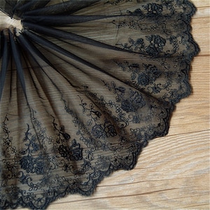 Könnte beinhalten: Schwarze Spitzenborte mit einem gewellten Rand und floraler Stickerei. Die Spitze ist zart und durchsichtig, und die Stickerei ist filigran.