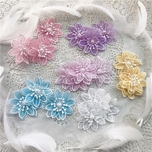 May include: A collection of multi-colored fabric flower appliques featuring sheer petals with embroidered edges and a central cluster of small white beads. The set includes pink, purple, blue, white, and yellow floral pieces arranged together.