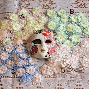May include: Assortment of delicate lace flower embellishments in various pastel colors, including pink, blue, and green. Each flower features a pearl center and is perfect for adding a touch of elegance to crafts and projects.