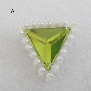 Może przedstawiać: Trójkątny, limonkowo-zielony kryształ górski z fasetowanym wzorem, otoczony obramowaniem z białych pereł.