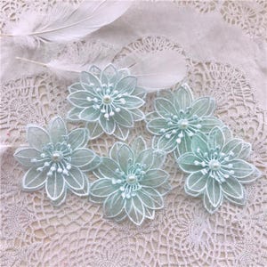 May include: Five light mint green floral appliques featuring layered sheer petals with white embroidered edges and a central white pearl bead accent. Each flower has multiple pointed petals arranged in a circular pattern with delicate stamens.
